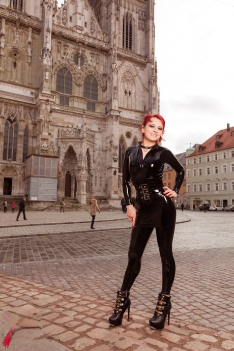 Sexiga rödhåriga Lara Larsen modellerar på en stadsgata i latexkläder och stövlar