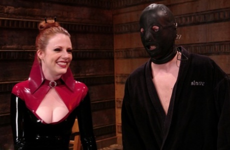 Rødhåret gudinde topper en hætteklædt mandlig slave iført latex