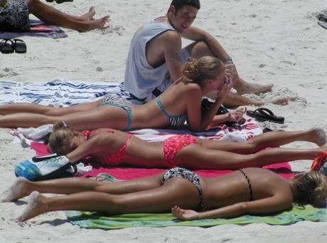 Candid action of amateur girls soaking up the rays on a beach in bikinis