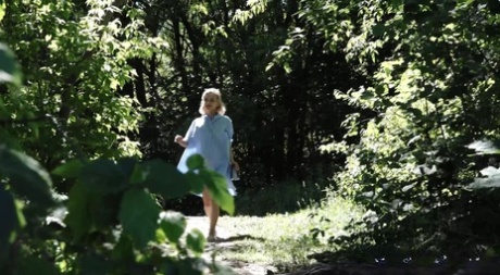 Lilla blonda Masha sitter på huk för ett brådskande piss vid buskarna vid Riverside