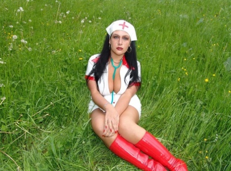 Enfermeira de cabelo escuro expõe as suas grandes mamas perto do bosque com botas de látex vermelhas