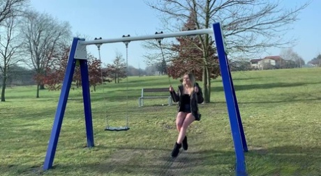 Blondes Küken Claudia Macc hebt ihren Rock an, um auf einer Schaukel zu pinkeln